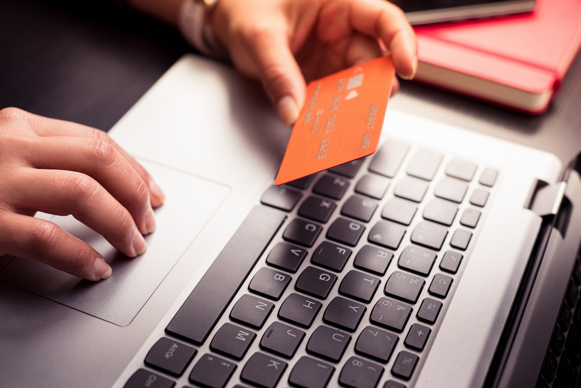 Pessoa segurando um cartão de crédito ao realizar uma compra no notebook